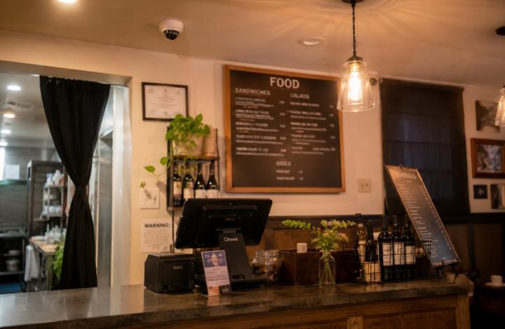 Clean, modern US restaurant interior — a small compact security camera mounted subtly above the POS/cash register area, blending naturally into the ceiling